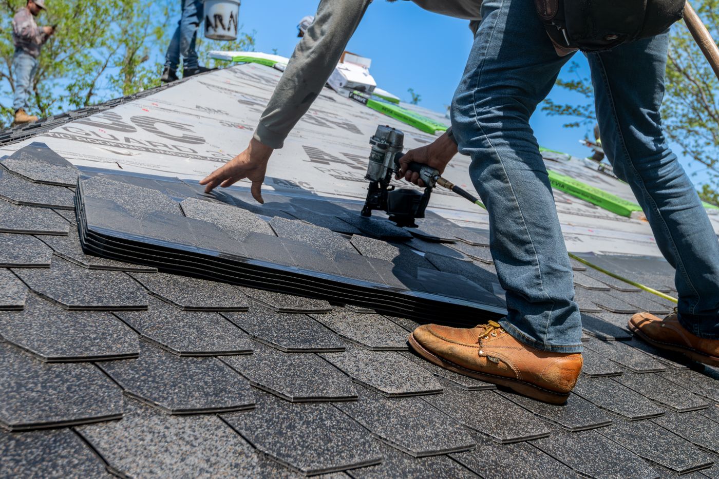 Roofer on a residential roof driving nails into new asphalt shingles with a nail gun